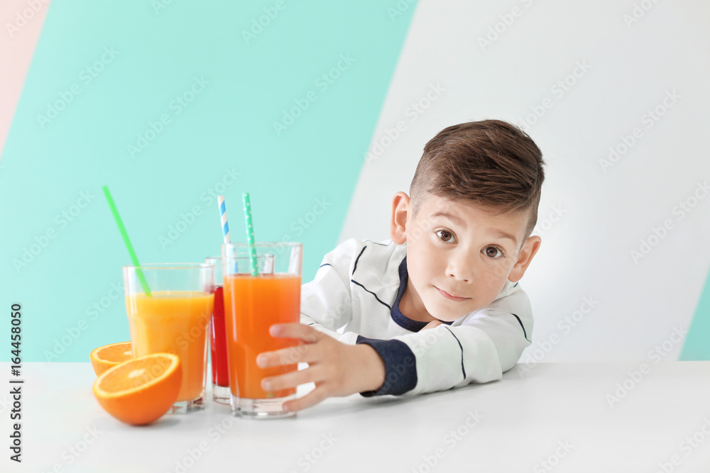 Cute little boy with glasses of juice sitting at table, on color background Cute little boy with glasses of juice sitting at table, on color background