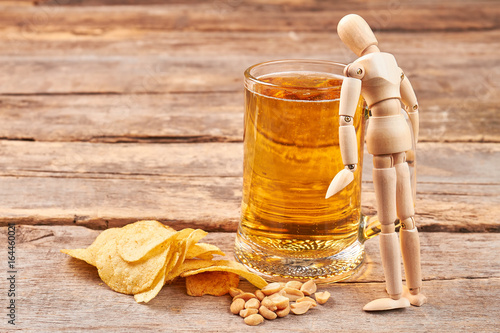 Human wooden dummy and glass of beer. Potato chips, nuts, glass of beer, human wooden dummy, wooden background. photo