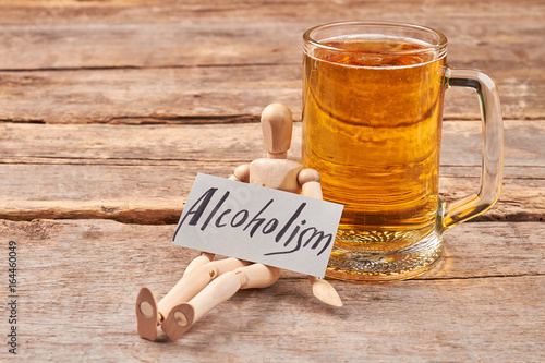 Alcoholism kills organism. Human wooden dummy with paper message near mug with beer. photo