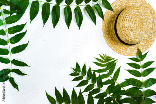 Green leaf branches and straw haton white background. flat lay, top view photo