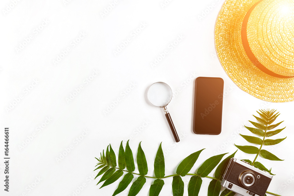 Straw hat with green leaves and old camera on white background, Summer background. Top view. Sun flare