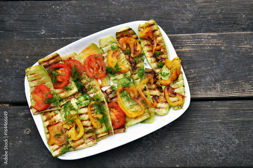 White rectangular dish with grilled zucchini and tomatoes on a rustic wooden brown surface.
