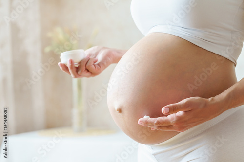 Pregnant woman aplying cream at her belly for prevention of stretch marks on the skin photo