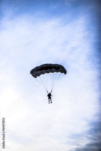 Silhouette of parachuter on a blue sky with clouds on it.