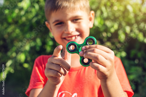 Fotografie A boy plays with spinner twisting it in his hand on outdoors