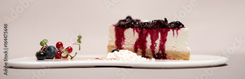 Fancy dessert with cheesecake and forest fruits,  on white plate, light brown background