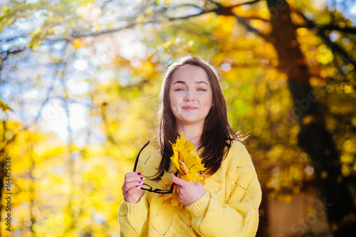 Beautiful woman with glasses and yellow leaves in hands with secret positive emotion over autumn yellow background Closeup portrait of long hair girl