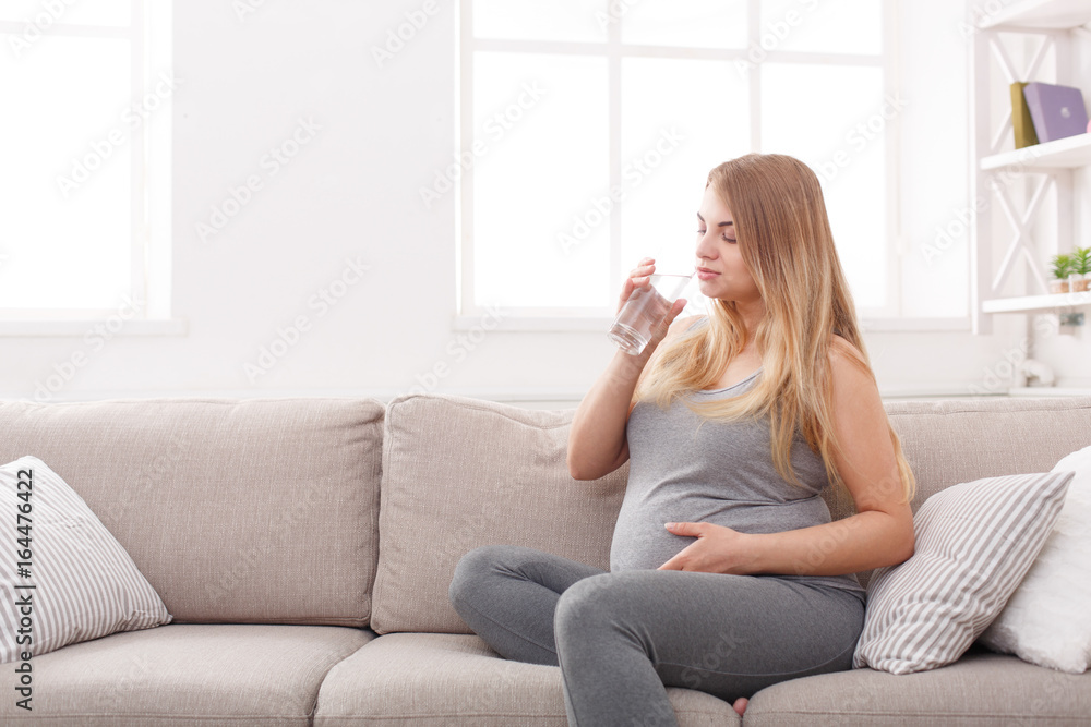 Pregnant woman with glass of water sitting on sofa Pregnant woman with glass of water sitting on sofa