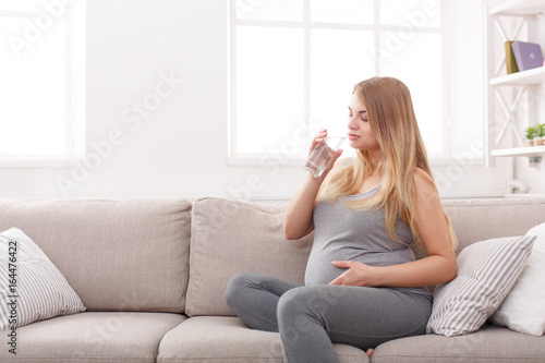 Pregnant woman with glass of water sitting on sofa © Prostock-studio