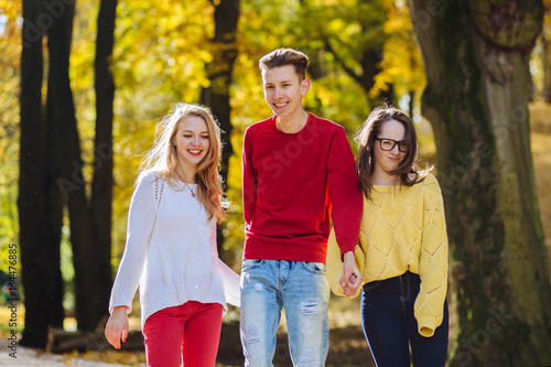 Education  lifestyle and people concept - young man in red shirt and two girls laughing and running over in autumn park.