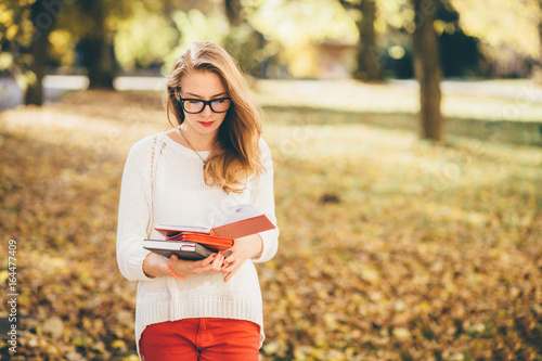 Young beautiful girl in glasses reading notebook in autumn park