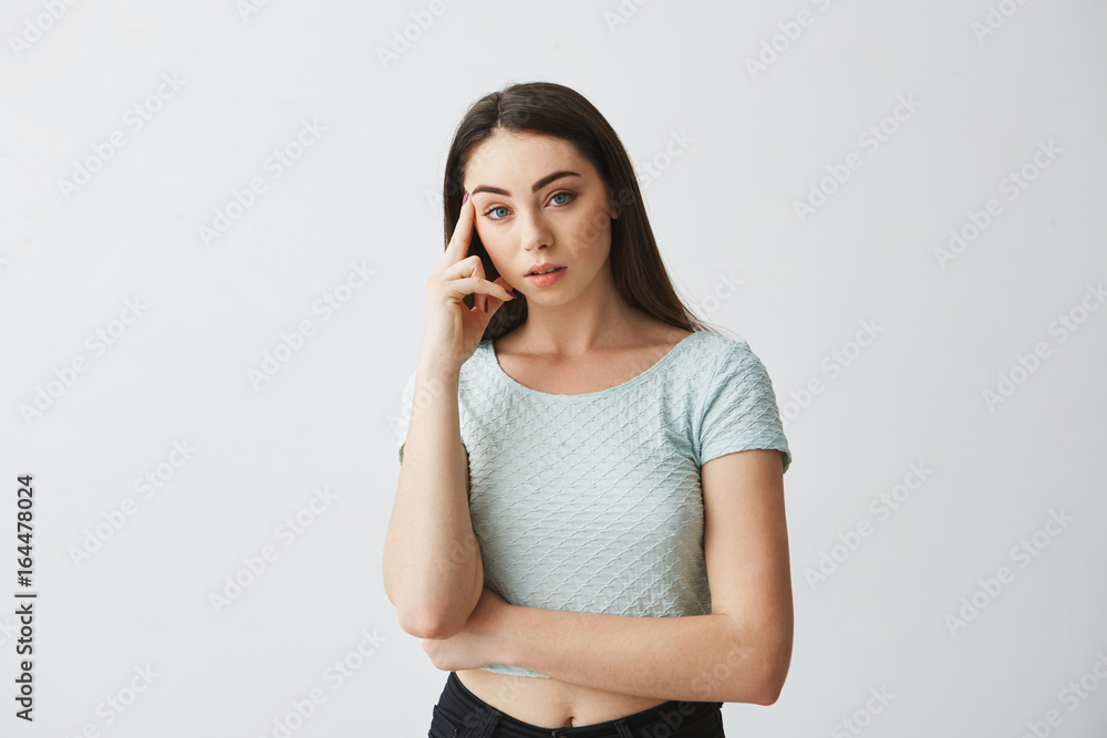 Portrait of young beautiful girl looking at camera thinking with finger on temple over white background. Portrait of young beautiful girl looking at camera thinking with finger on temple over white background.