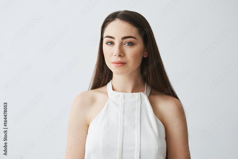 Portrait of young beautiful tender girl in blouse looking at camera smiling over white background.