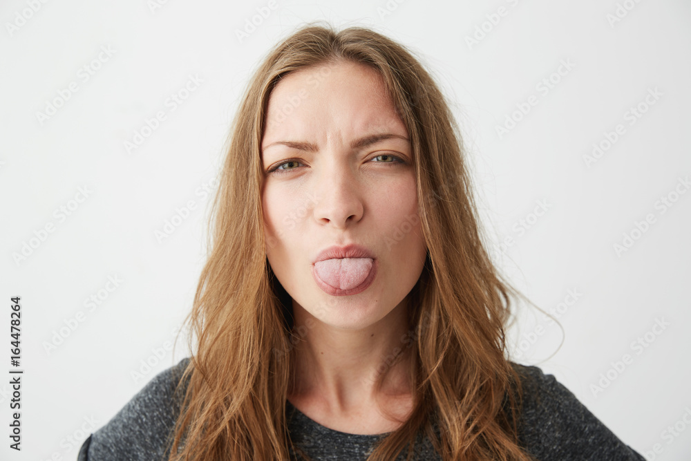 Portrait of young pretty funny girl looking at camera showing tongue over white background.