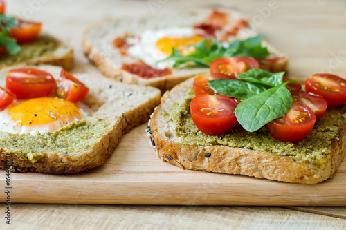 Breakfast toasts with multicereal bread, pesto sauce, cherry tomatoes, eggs, spinach on wooden cutting board. Healthy breakfast. Balanced meal