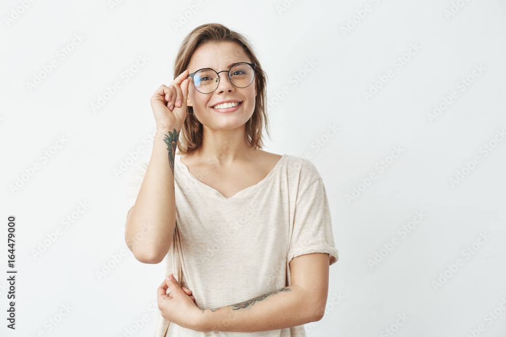 Young pretty girl smiling looking at camera correcting glasses over white background. Young pretty girl smiling looking at camera correcting glasses over white background.