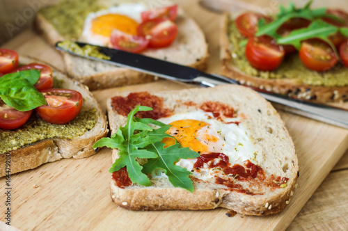 Healthy balanced toasts with egg, arugula, red cherry tomatoes, spinach leaves, pesto and tomato sauce and multicereal bread. Healthy breakfast sandwiches