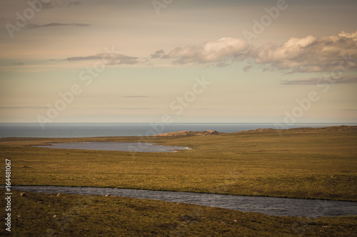 Assynt Peninsula, Scotland - June 7, 2012: Flat land with dry vegetation and cut by creek and lake descends to Atlantic Ocean. Twilight sky with white clouds at Brae of Achnahaird. Total desolation.