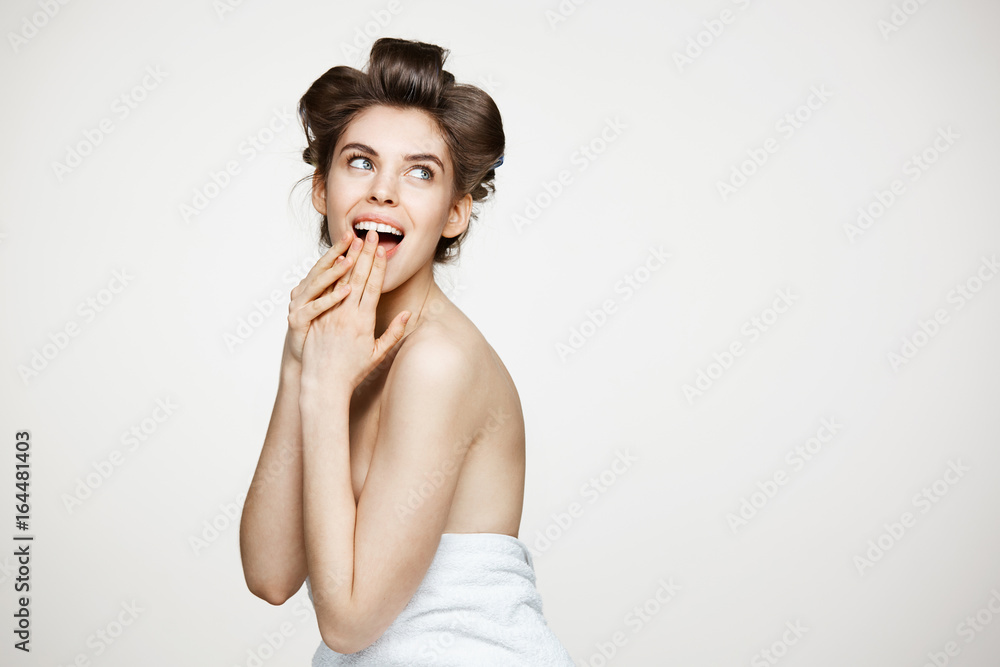Surprised young beautiful girl in hair curlers smiling with opened mouth over white background. Beauty and spa concept. Surprised young beautiful girl in hair curlers smiling with opened mouth over white background. Beauty and spa concept.