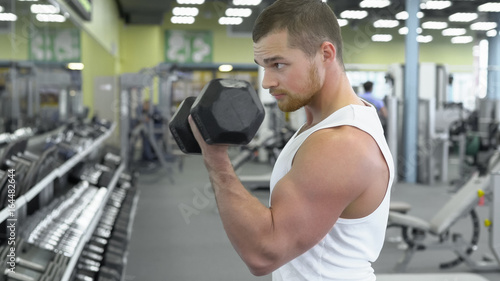 Portrait of strong athletic man at the gym training. bodybuilder does an exercise on the biceps with dumbbells