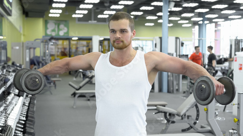 Portrait of strong athletic man at the gym training. bodybuilder does an exercise for shoulders with dumbbells