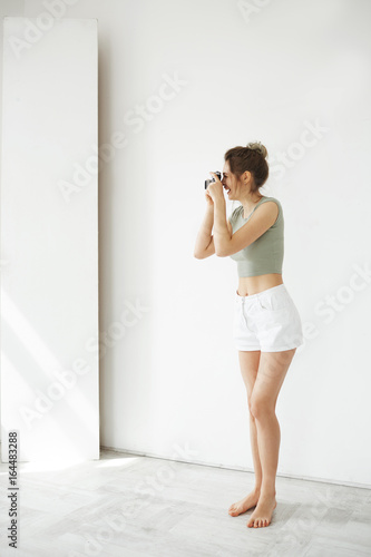 Portrait of cheerful happy young female photograph smiling taking picture on old camera over white wall.