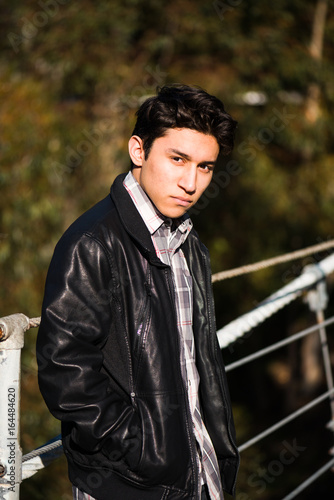 Young hispanic male sitting on a suspension bridge; posing, outdoors