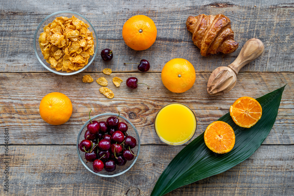 Light summer breakfast. Muesli, oranges, cherry and croissant on wooden table background top view