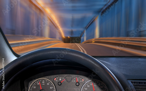 A view of the cockpit of a car driving at night through an illuminated bridge