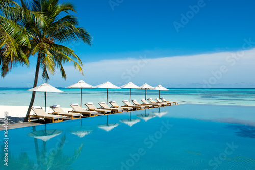 Fototapeta Naklejka Na Ścianę i Meble -  Large infinity pool on the shores of the Indian Ocean with sunbeds and umbrellas in the shade of the palm trees