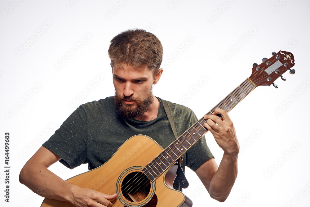 Obraz premium Young guy with a beard on a light background playing the guitar