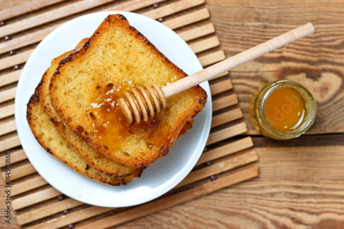 Fried toast on a white plate with a jar of honey and a spoon on a wooden background photo