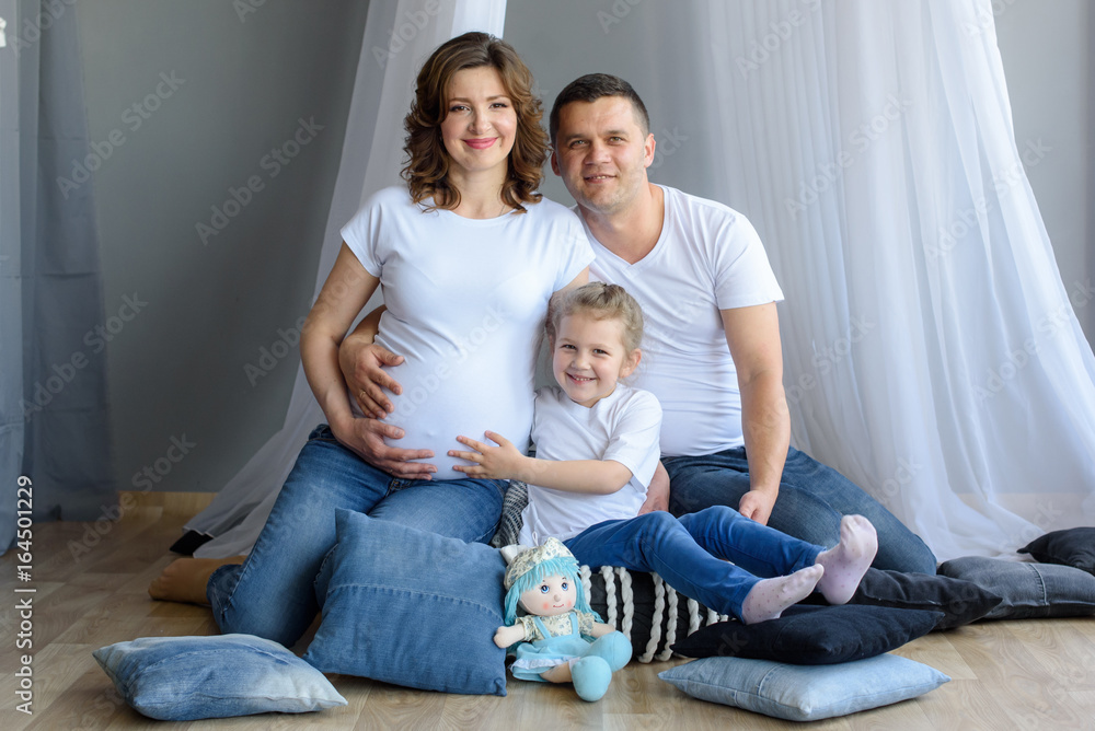 Pregnant family with little child girl is hugging at home. A happy family is waiting for the birth of a newborn baby 