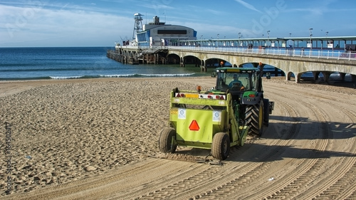 Fototapeta Naklejka Na Ścianę i Meble -  A tractor cleans the sand by raking it and picking up debri on the beach  at the english seaside town of Bournemouth