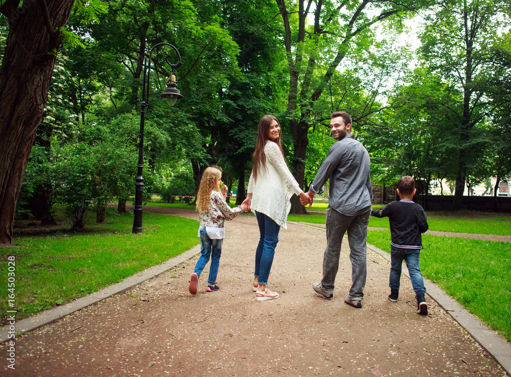 Happy family walking holding hands in green city park