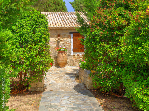 View on family Greece traditional Greek village style hotel entrance green gate  antique classical vase jar flowers. Gingerbread Classic Greece architecture Greece holidays vacations sightseeing tours