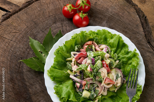 Fresh salad with fresh red cerry tomatoes, cucumbers, chicken, red onion, radish, bell pepper, lettuce with special spisy sauce on wooden table. Healthy eating and diet concept.