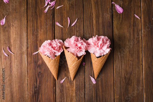 Fototapeta Naklejka Na Ścianę i Meble -  Flowers in a waffle cone. Pink carnations. Flowers on a wooden  background. Copyspace. Flower photo concept