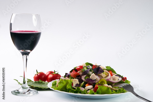 Healthy fresh vegetable salad with chicken meat next to fork and glass of red dry wine isolated on white background with copy space. Healthy eating and detox concept