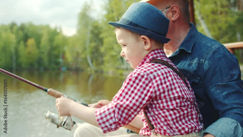 Little boy is turning fishing reel on fishing with his grandfather at the lake Little boy is turning fishing reel on fishing with his grandfather at the lake