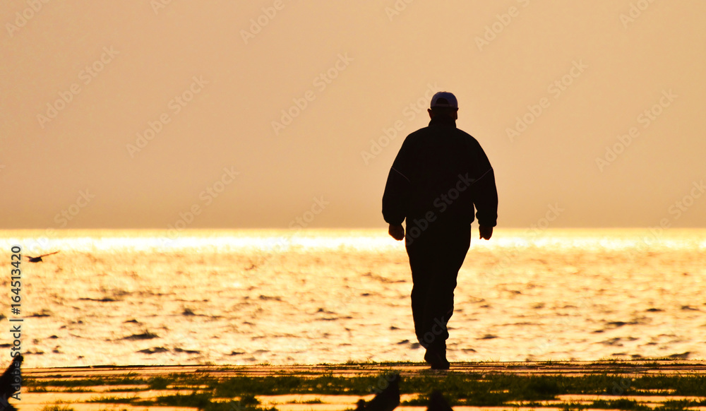 Old man walking alone on the seashore at sunset, silhouette. Old man walking alone on the seashore at sunset, silhouette.