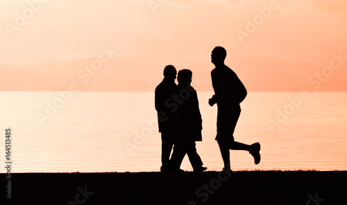 Old couple walking near the sea at sunset. A man running on the seashore, silhouette. 