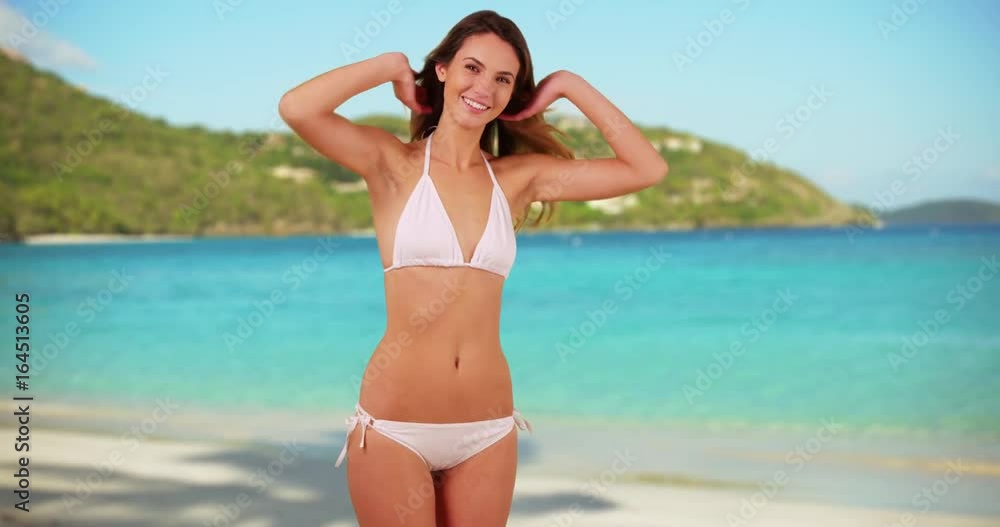 Portrait of young Caucasian woman modeling white bikini on beach in the Caribbean. Attractive female playing with hair and smiling at camera enjoying vacation on Virgin Islands. 4k Portrait of young Caucasian woman modeling white bikini on beach in the Caribbean. Attractive female playing with hair and smiling at camera enjoying vacation on Virgin Islands. 4k
