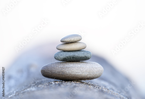 Four smooth beach stones stacked and balanced on a driftwood log