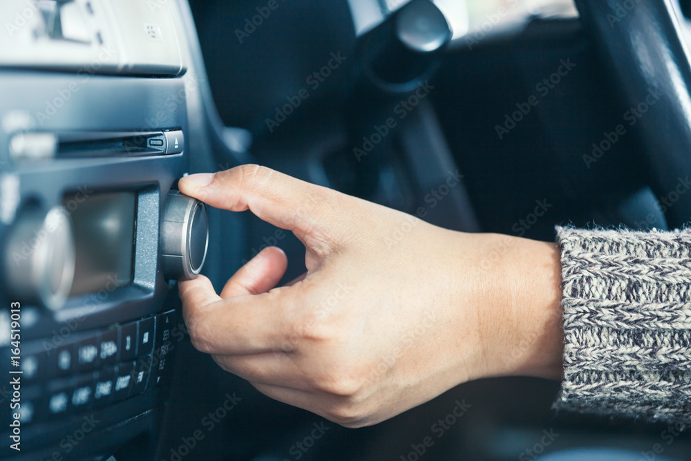 Woman hand adjusting the sound volume of car radio while driving a car in vintage color tone
