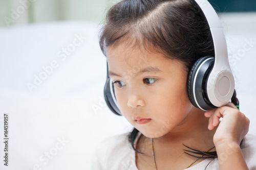 Cute asian child girl in headphones listening the music in her room
