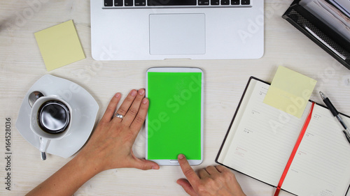 
woman using a mobile phone / tablet PC with green screen at her desk in the office - top view photo