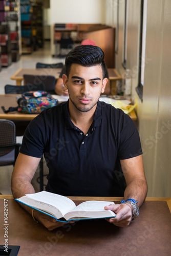 Canvas Print Handsome male college student sitting in the university library, studying a book