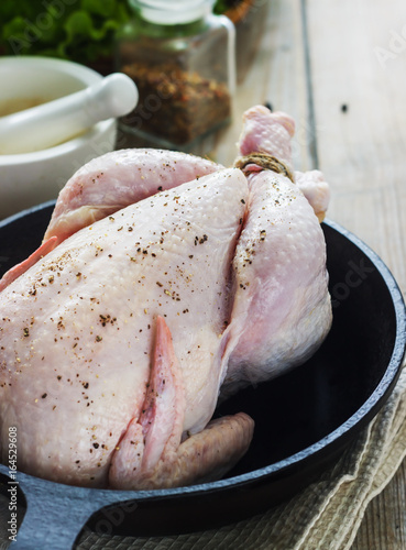 Raw chicken on a cast-iron frying pan on a wooden background