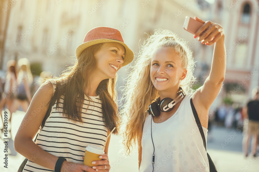 Two happy women are having nice time together in the city. They are taking selfie. 